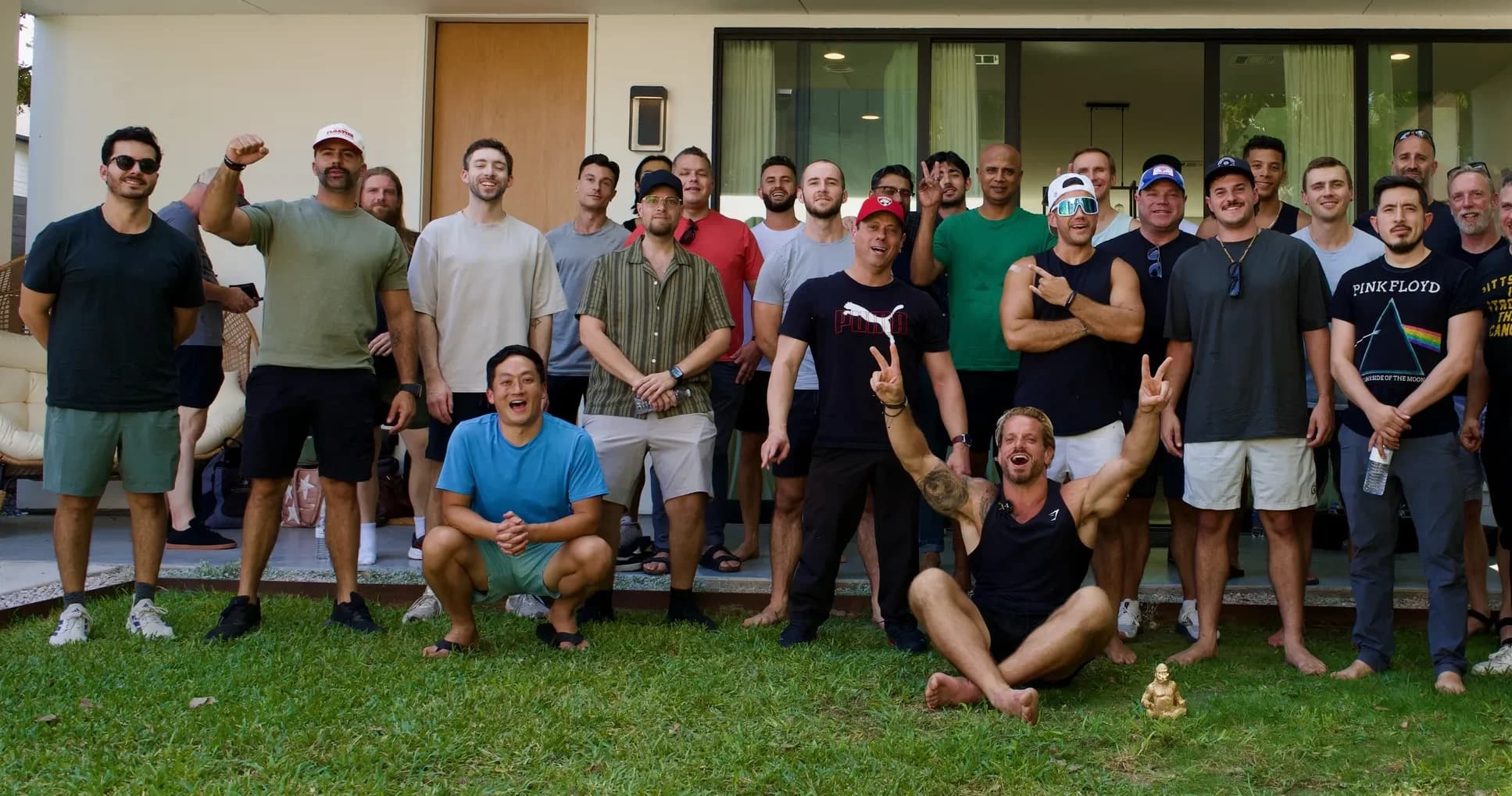 Jarred Curcio seated on the ground giving a peace sign with the crew behind him at a house in Austin, Texas